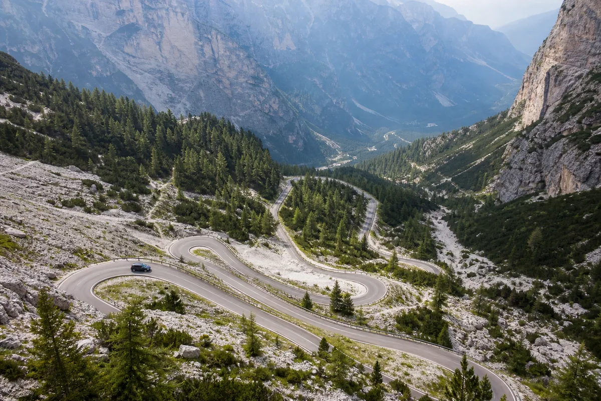 Route de montagne en lacets vers un col des Dolomites, vue en plongée sur les épingles et les sapins
